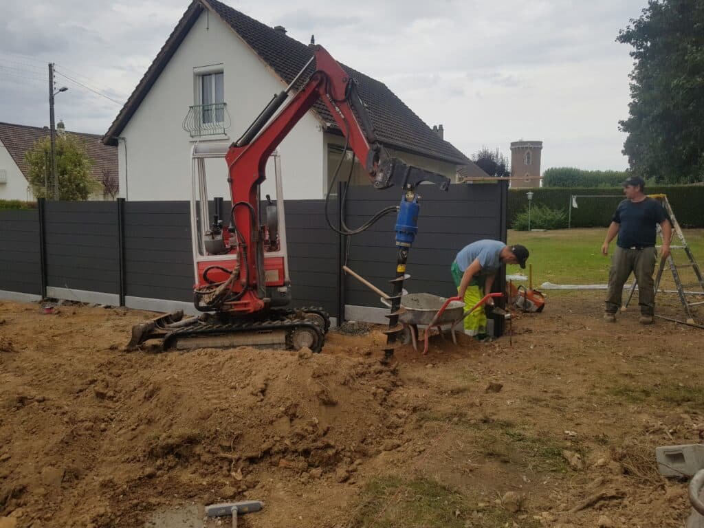 Travaux d'installation de clôture avec une mini-pelle et deux ouvriers