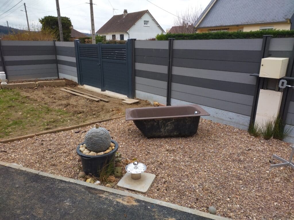 Clôture moderne en panneaux gris avec un portail assorti, entourant un espace jardin en cours d'aménagement.