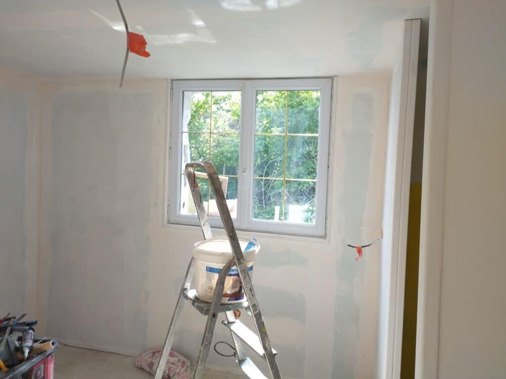 Pièce en cours de rénovation avec une échelle et des outils de peinture.