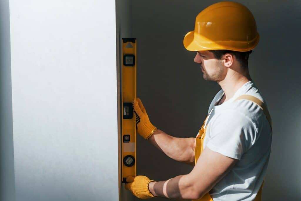 Un homme à tout faire en uniforme jaune vérifie les niveaux du mur. Conception de rénovation de maison