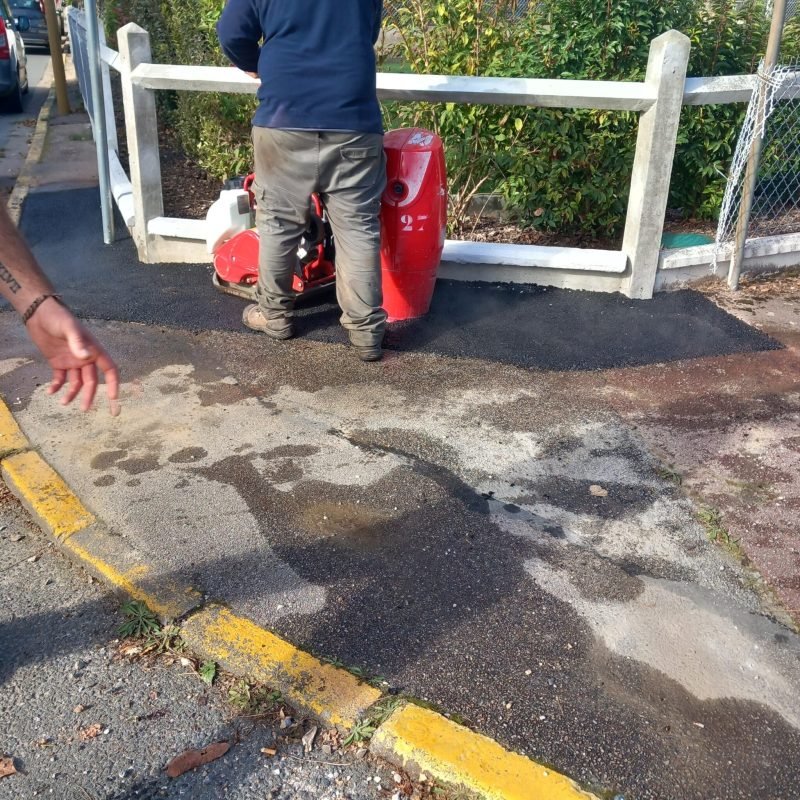 Un ouvrier effectuant le compactage d'une zone d'enrobé avec une machine près d'une bordure jaune.