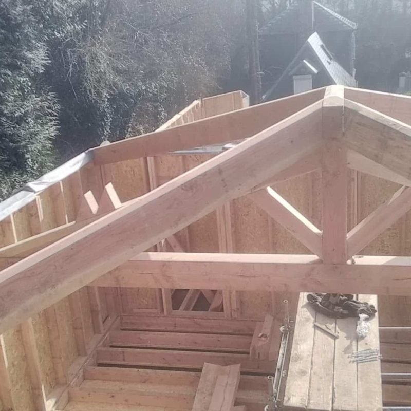 Charpente de toit en bois avec support en cours de montage sur un bâtiment.
