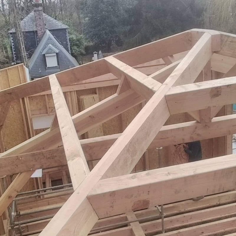 Charpente en bois d'un toit en cours de construction, montrant les poutres croisées au sommet d'une maison en construction.