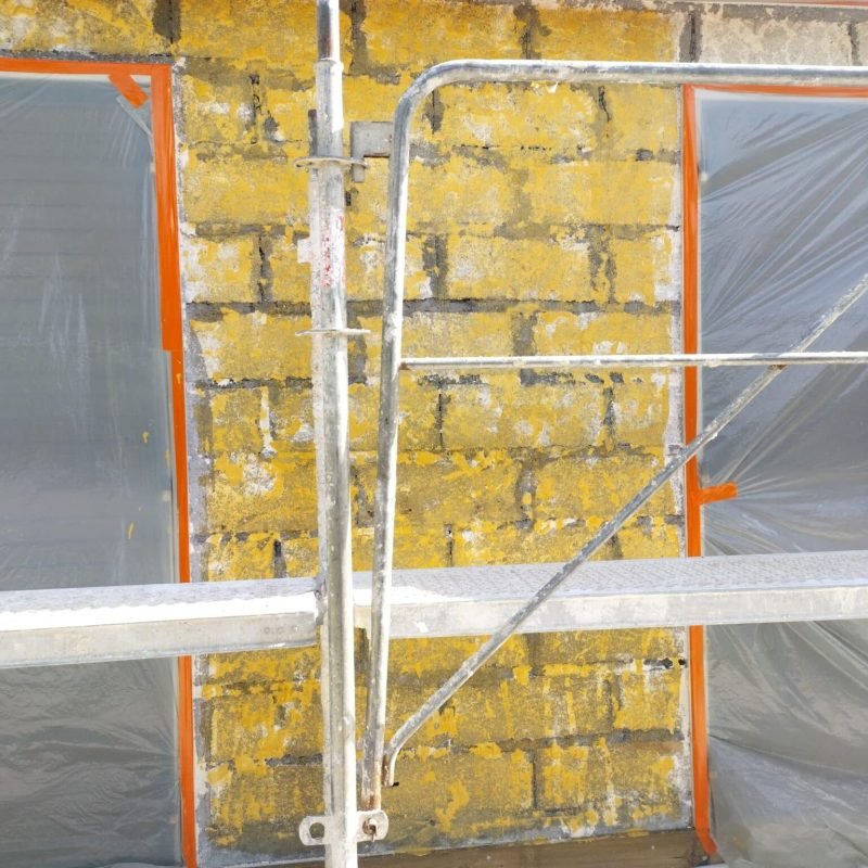 Mur en pierre jaune avec l'enduit enlevé et fenêtres protégées par du plastique, en cours de rénovation