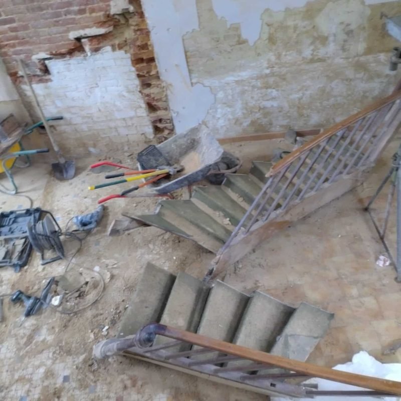 Détail d'une ouverture murale avec des gravats au sol et des outils de chantier, dans le cadre de la réhabilitation d'un espace intérieur.