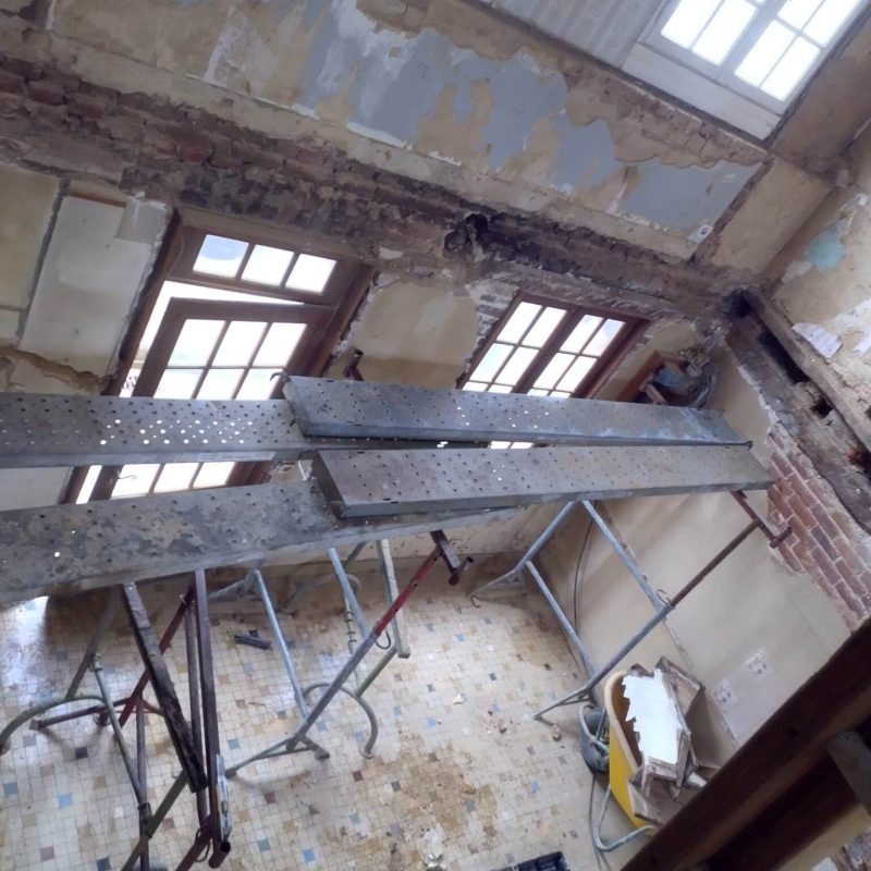 Intérieur d'une pièce avec échafaudage pour travaux de rénovation, montrant un mur abîmé et un plafond à réparer.