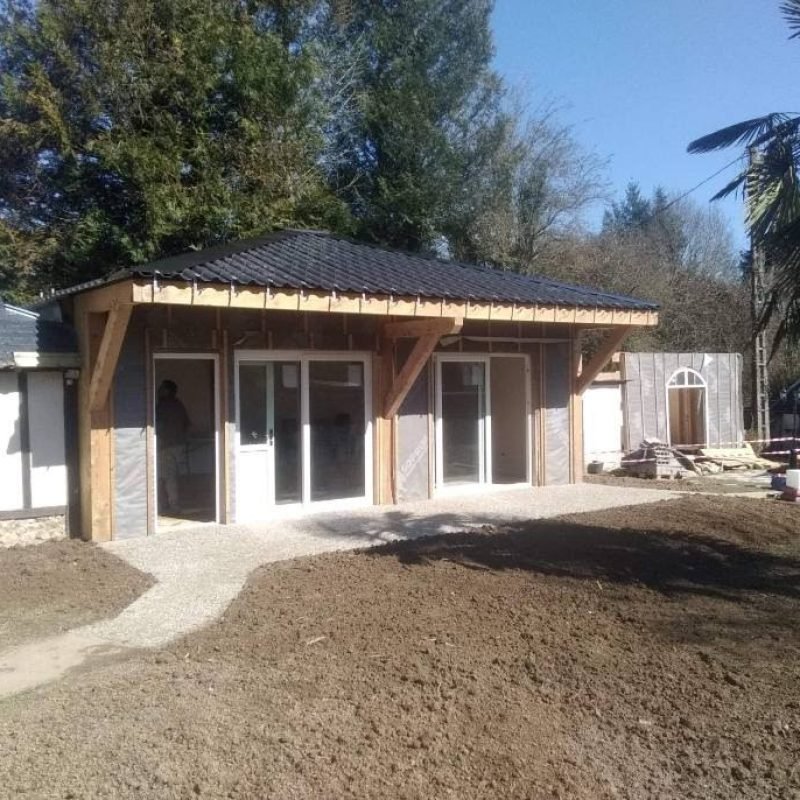 Vue extérieure d'un bâtiment en bois avec une terrasse en gravier devant, dans un environnement verdoyant